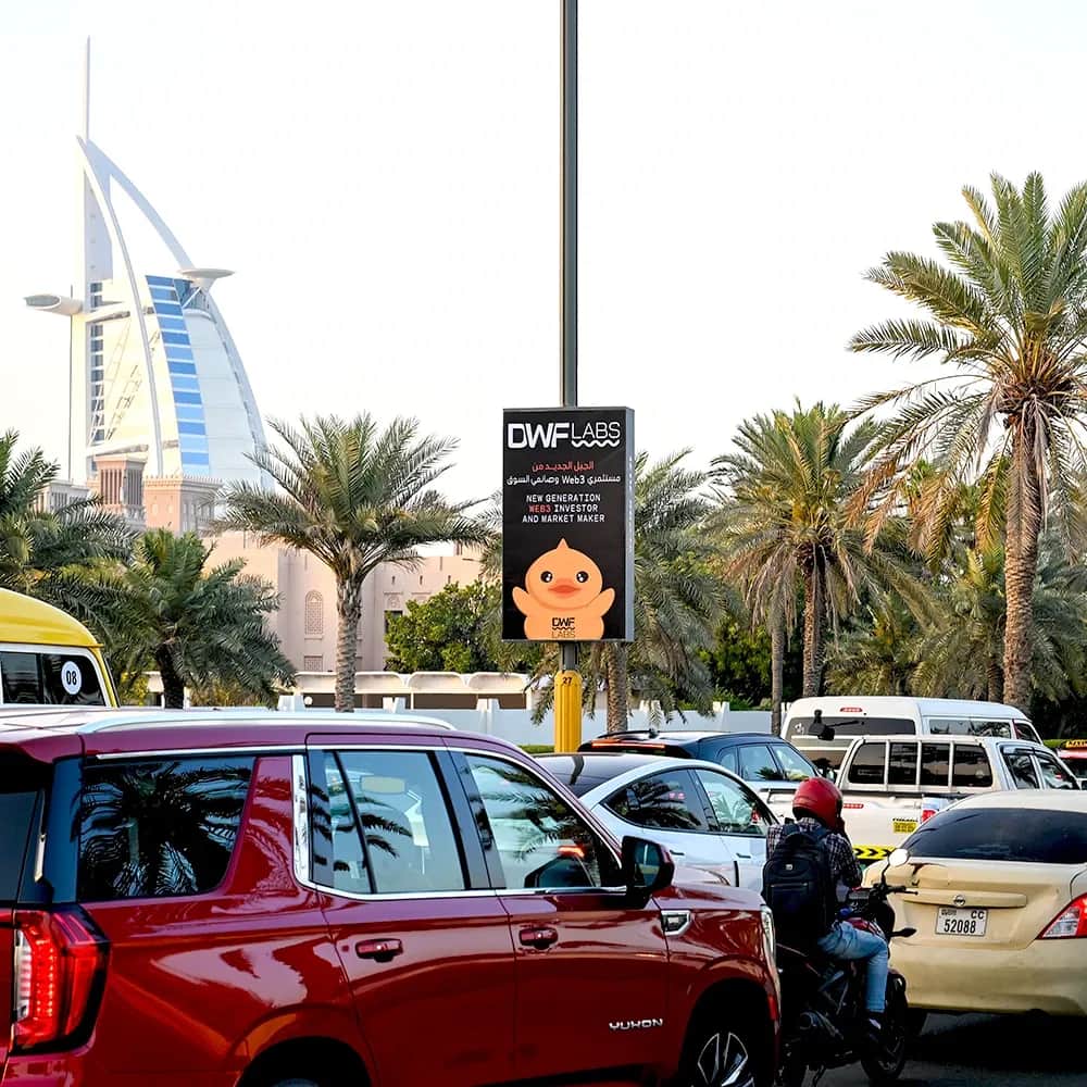 DWF Labs lamppost advertising campaign near Burj Al Arab, Dubai — vertical roadside streetlight banner promoting Web3 investor and market maker brand in high-traffic urban location with palm trees and vehicles.